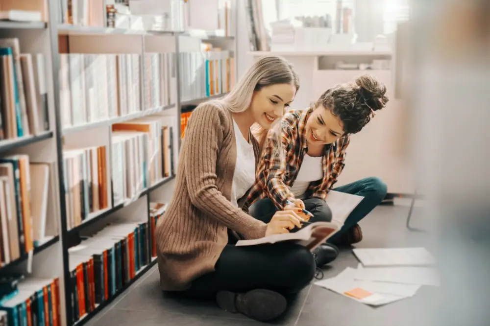 Two women siting on the floor reading a book